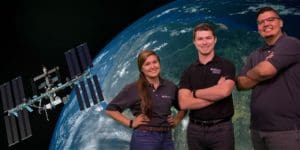 Photo of Dakotah, Alexis, Vince in front of an image of satellite orbiting the Earth.