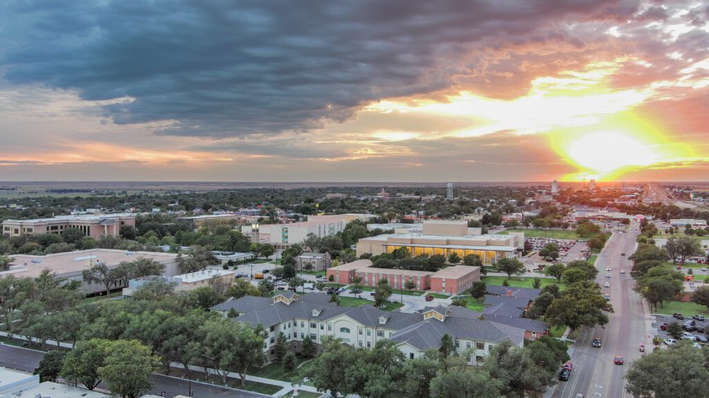 Aerial view of a campus and town at sunset beneath dramatic clouds and bright evening sunlight.