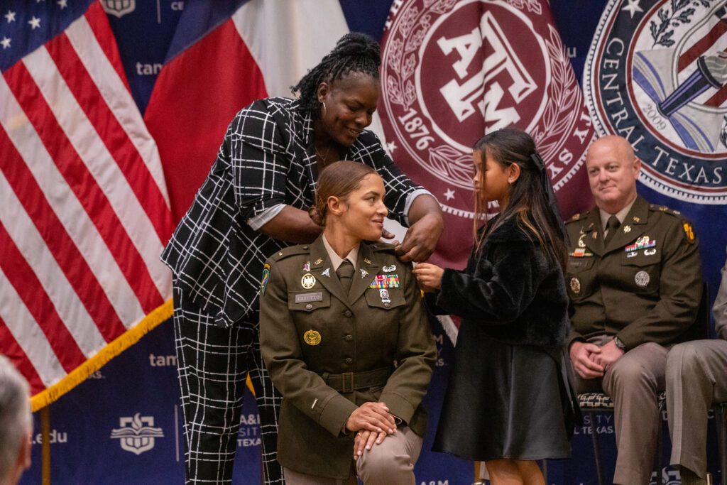 A uniformed cadet receives insignia from a woman and young child during a commissioning ceremony.